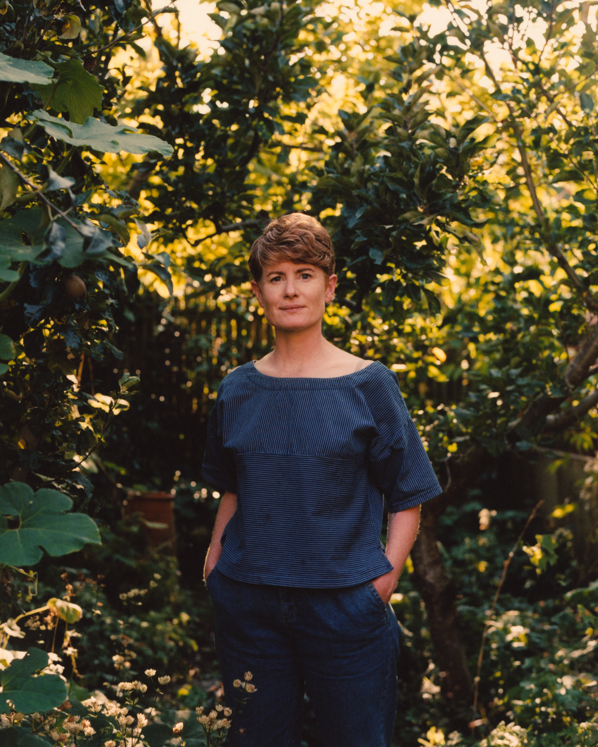 A lady stands outside amongst bushes