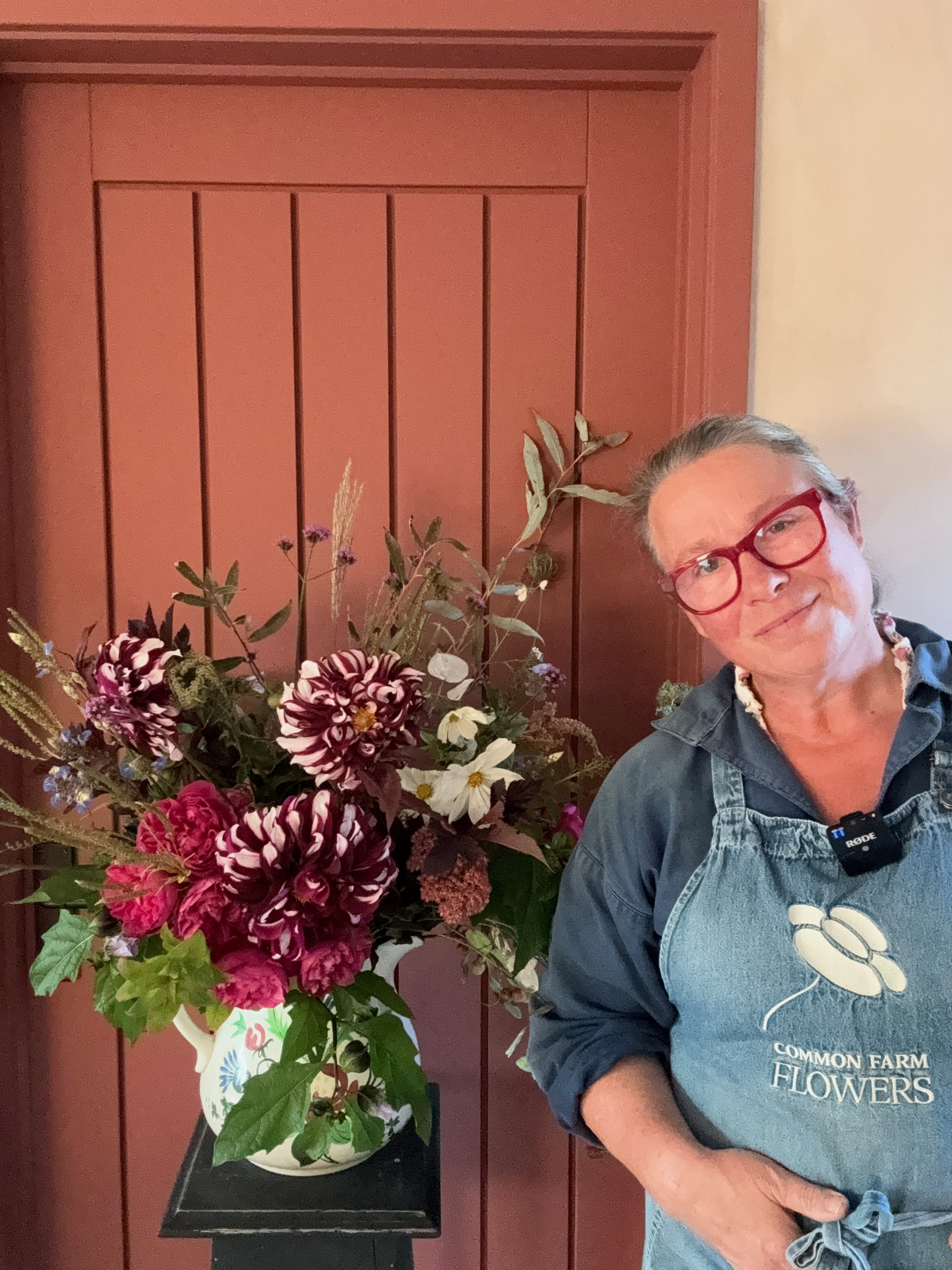 A lady standing smiling next to a vase of flowers